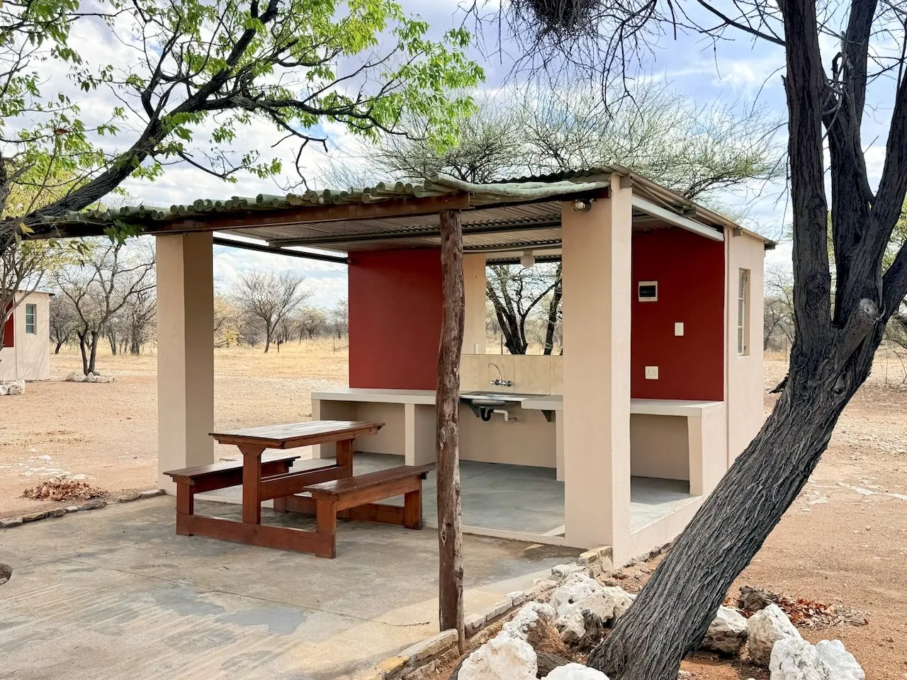 Shaded campsite shelter with a picnic table and braai